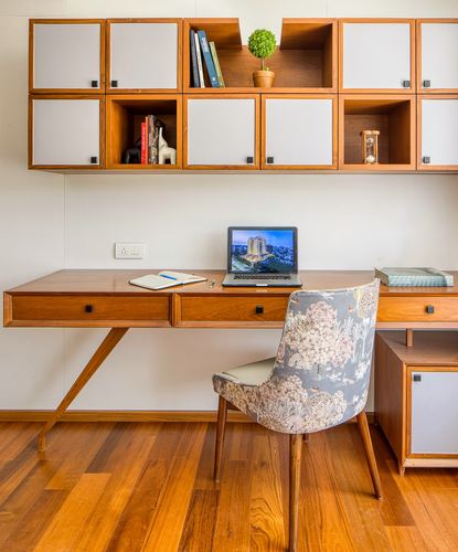 Wood study desk with laptop beneath white and wood cubby shelving, floral chair, wood floor