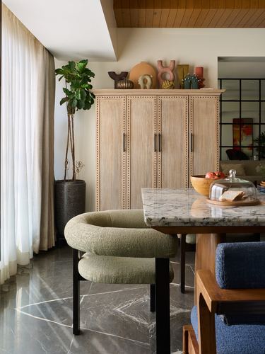 Dining nook with sage boucle chair, marble table, studded wooden cabinet and fiddle leaf fig