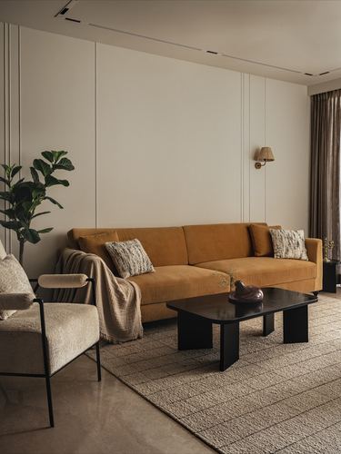 Living room with mustard velvet sofa, black coffee table, and boucle armchair against paneled wall