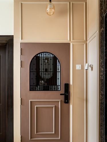 Mauve entry door with arched iron grille window, framed by cream panelled wall and dark stone strip.
