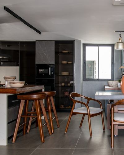 Dark kitchen with wooden bar stools, glass cabinets, and adjoining dining area near a window