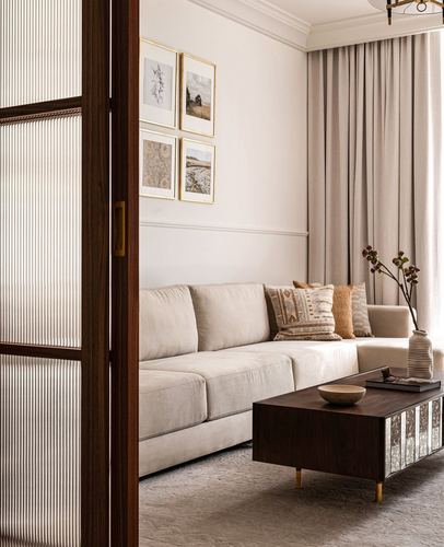 Living room seen through a reeded glass door, beige sofa, dark wood coffee table, framed art wall