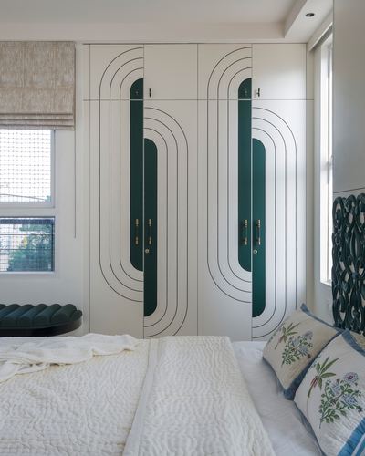 Bedroom with art deco wardrobe featuring teal and ivory arched line motifs, carved headboard, textured bedding