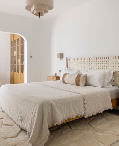 Neutral bedroom with woven headboard, arched doorway, and layered white linens