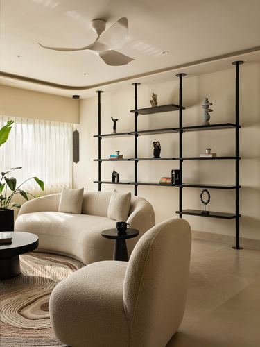 Ivory living room with curved boucle sofa and black open shelving unit against wall