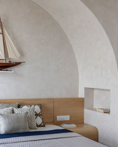 Curved plaster archway above a wooden headboard bed with a model sailboat display