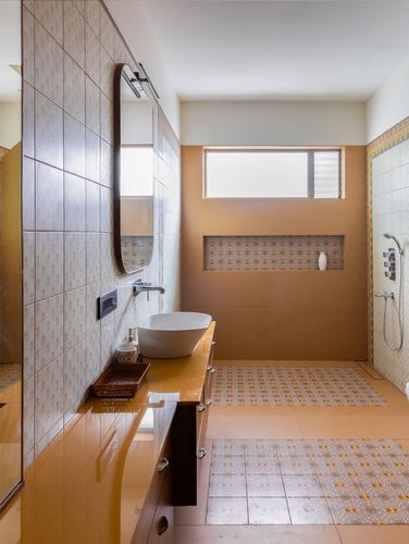 Ochre-toned bathroom with vessel sink, wooden vanity, and patterned tile niche and floor accents