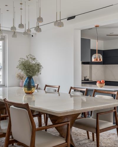 Marble-top dining table with wood chairs, pendant lights, open kitchen beyond