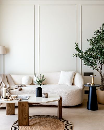 Cream boucle curved sofa against paneled wall with wood coffee table and olive tree