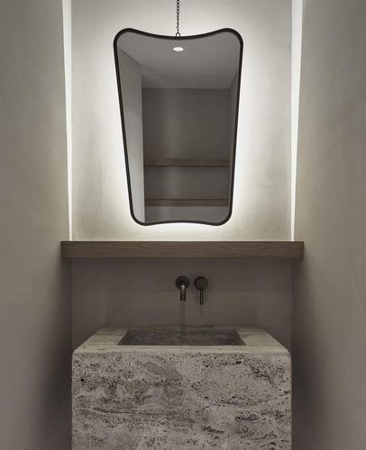 Backlit mirror above a rough-hewn stone basin in a minimalist plaster bathroom