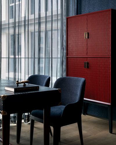 Red fluted cabinet beside navy chairs and dark table near sheer-curtained window