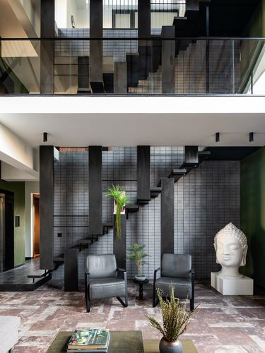 Double-height living room with black steel staircase, tiled wall, buddha sculpture and leather armchairs