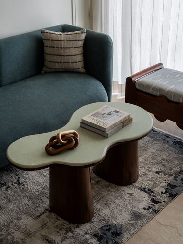 Kidney-shaped stone-top coffee table with wooden legs beside a teal sofa and bench