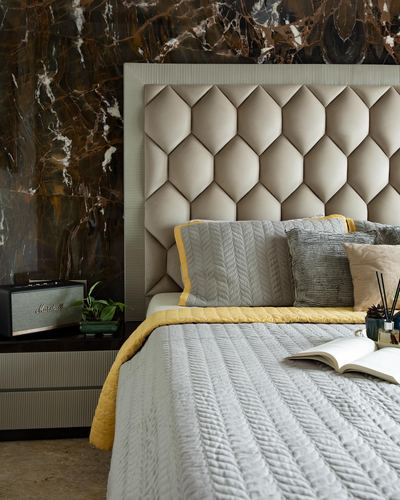 Bed with geometric tufted headboard against dark marble wall, grey and mustard bedding