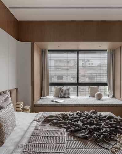 Bedroom with wood-panelled window seat overlooking city buildings, bed with textured throws in foreground
