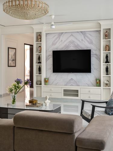Living room with bookmatched marble-look tv wall flanked by curio shelves and crystal chandelier