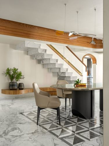 Marble-clad floating staircase beside round dining table on patterned marble floor
