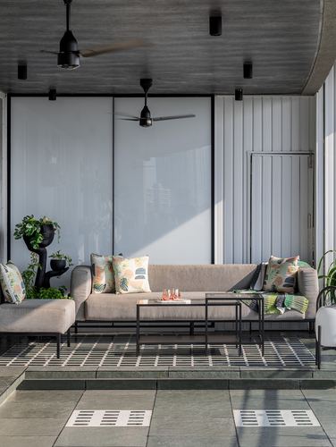 Covered terrace lounge with sectional sofa, patterned cushions, black metal tables and ceiling fans, stone flooring.