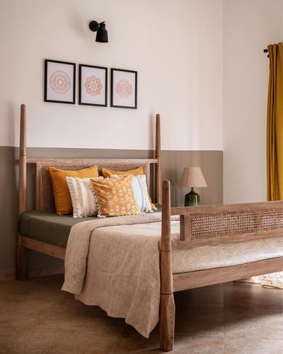 Wooden four-poster bed with cane headboard, mustard cushions, and framed mandala prints on a two-tone wall.