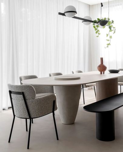 Oval stone-topped dining table with conical base, bouclé chairs, black bench and sculptural pendant light