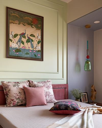 Bedroom corner with pink velvet headboard, floral pillows, peacock painting and fluted wall niche with pendant light
