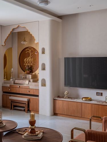 Pooja alcove with arched mirror and carved motif beside a living room TV console