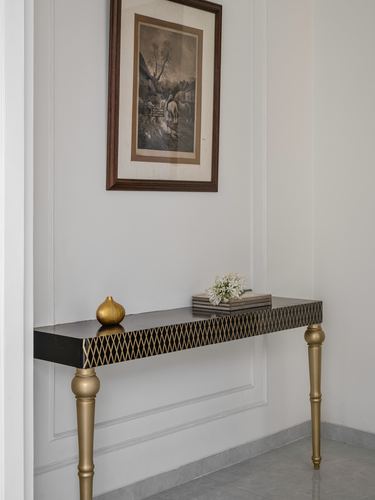 Narrow console table with brass diamond inlay under framed vintage print on paneled wall