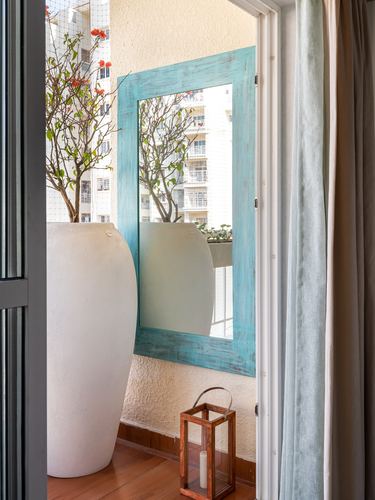 Balcony nook with white planter, potted plant, turquoise mirror reflecting building view, and lantern.