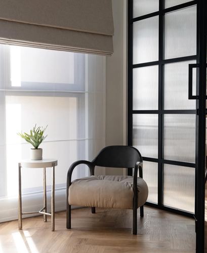 Black metal armchair beside window with sheer curtains and fluted glass door
