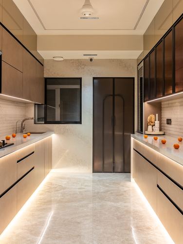 Symmetrical galley kitchen with beige stone counters, wood cabinetry and arched dark door at end
