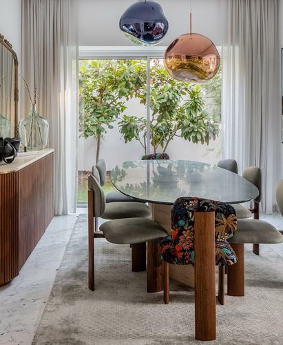 Oval glass dining table with mixed grey and floral chairs beneath two metallic globe pendants