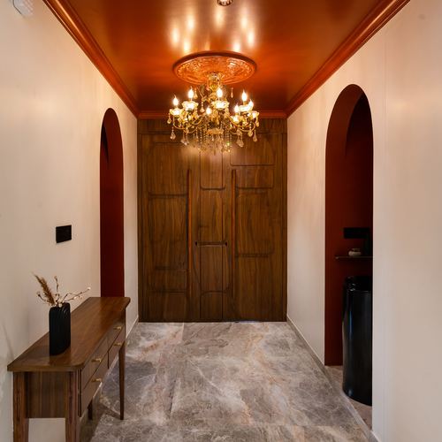 Foyer passage with glossy copper ceiling, brass chandelier, carved wood doors and marble flooring
