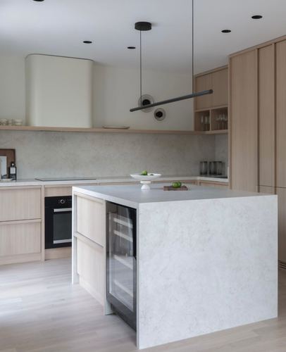 Minimalist kitchen with waterfall stone island, light wood cabinetry, and sculptural pendant light