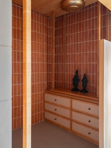 Pooja alcove with terracotta tile walls, wooden posts, storage cabinet, and two dark metal deity idols