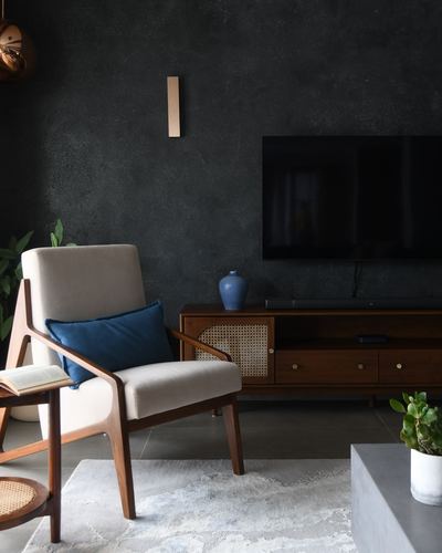 Cane-backed wooden armchair with blue cushion beside dark TV console against charcoal plaster wall