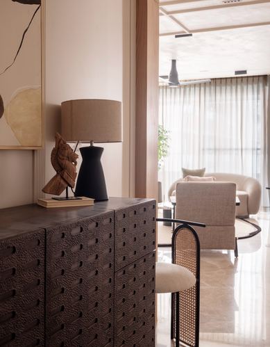 Textured dark sideboard with lamp and sculpture, opening to a curved beige living room beyond