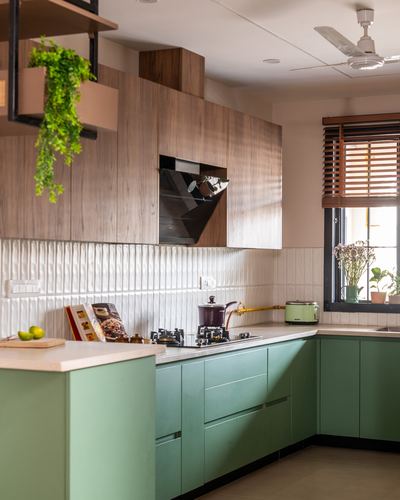 L-shaped kitchen with sage green cabinets, wood-textured upper units, ribbed white backsplash and window with wooden blinds