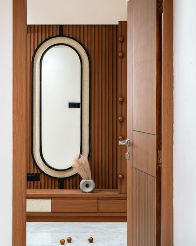 Foyer with fluted wood wall, oval cane-framed mirror, and wooden console seen through open door