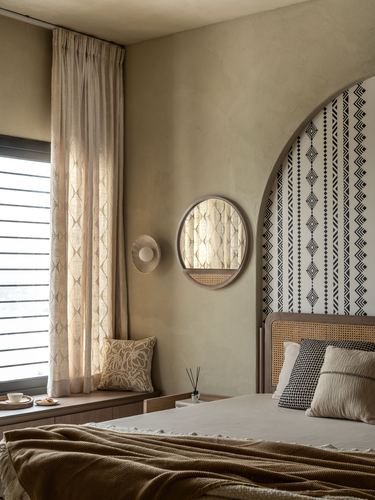 Bedroom with arched patterned niche, cane headboard, round mirror and curtained window seat
