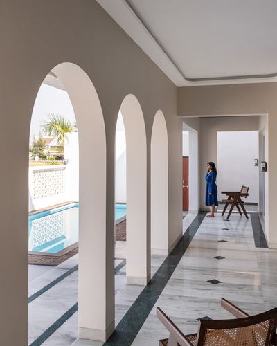Woman in blue stands in marble corridor beside arched colonnade overlooking pool, Raipur home