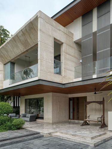 Cantilevered stone facade of a modern Ahmedabad villa with wooden swing and porch below