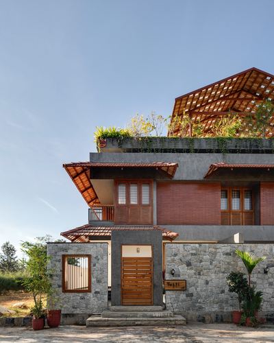 Multi-level stone and brick house facade with sloped tiled roofs and a rooftop wooden pergola under blue sky