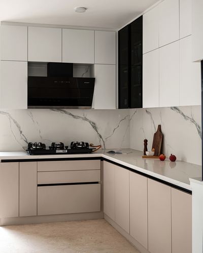 White and beige L-shaped kitchen with marble-look backsplash, black chimney hood, and styled countertop.