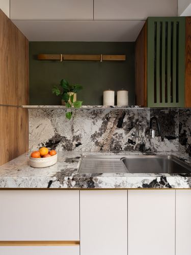 Kitchen counter with veined stone backsplash, steel sink, brass tap, and green fluted cabinet accent