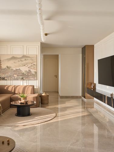 Sunlit neutral living room with sectional sofa, round rug, marble floor and wall-mounted television