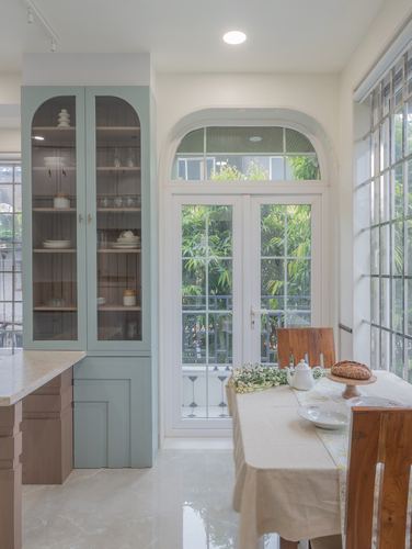 Sage green glass cabinet beside arched white door opening to garden, dining table set in foreground