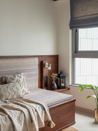 Wooden bed with patterned upholstered headboard beside a window with a black roller shade in a warm-toned bedroom