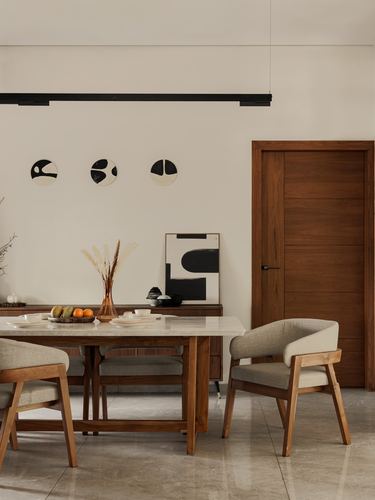Dining room with marble-top wooden table, cane-armed chairs, and walnut door under a linear pendant light