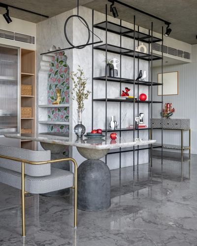 Dining table with marble top on sculptural base beside black shelving unit displaying curios