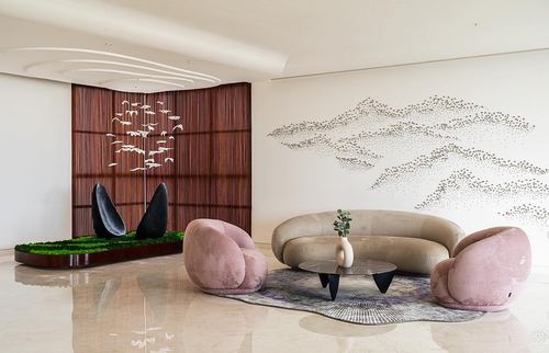Living room with curved beige sofa, pink armchairs, and bird mural wall behind slatted wood screen